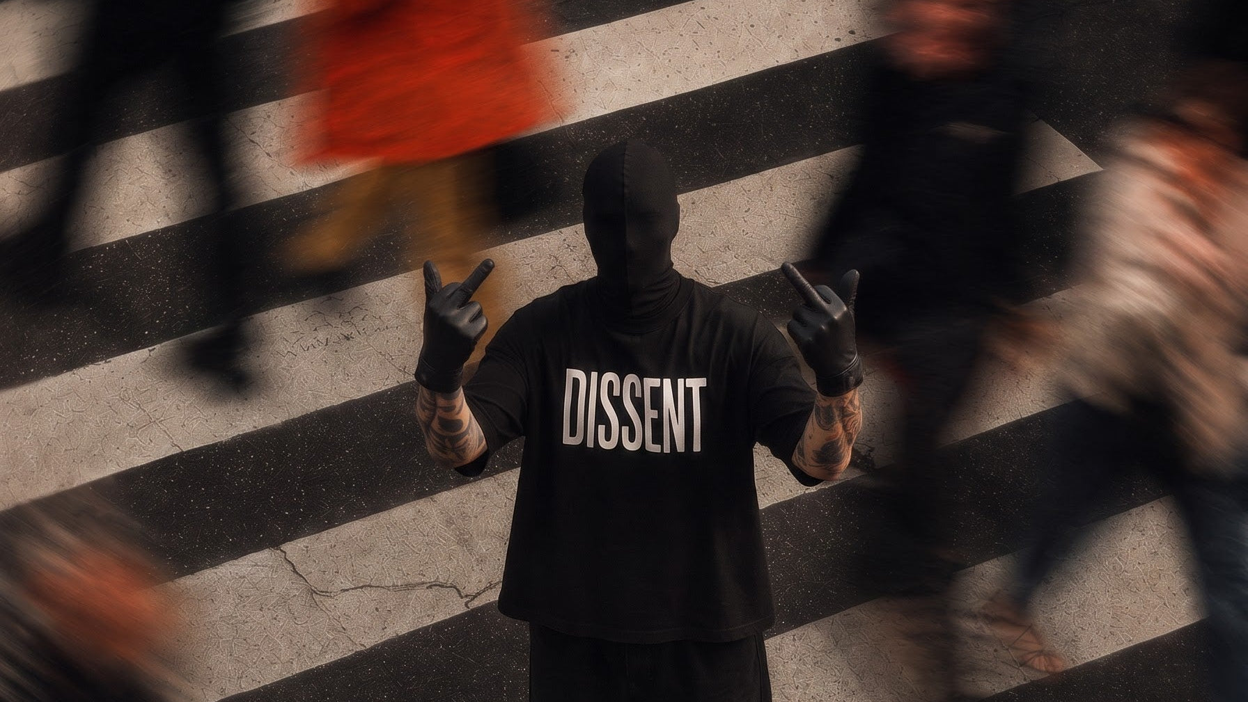 A person standing on a crosswalk wearing a black hoodie with the word 'DISSENT' printed in white across the back, surrounded by blurred pedestrians in an urban street scene.
