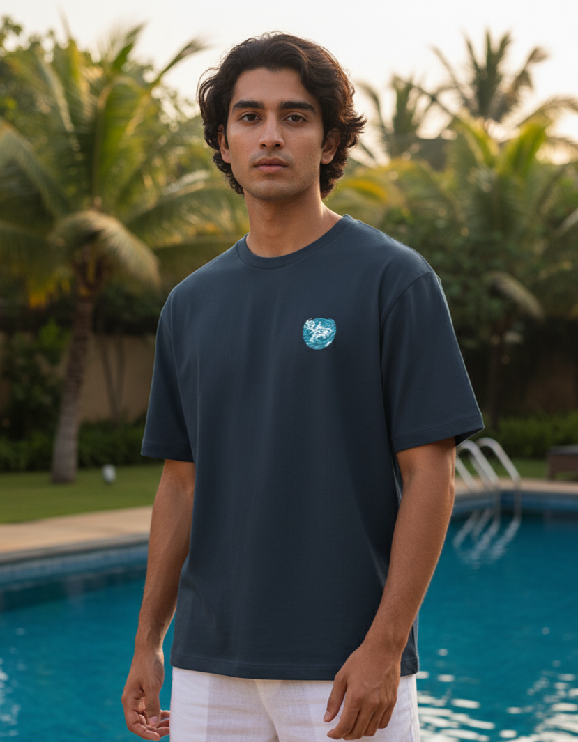 Man wearing a navy blue t-shirt with a logo standing by a pool with palm trees in the background